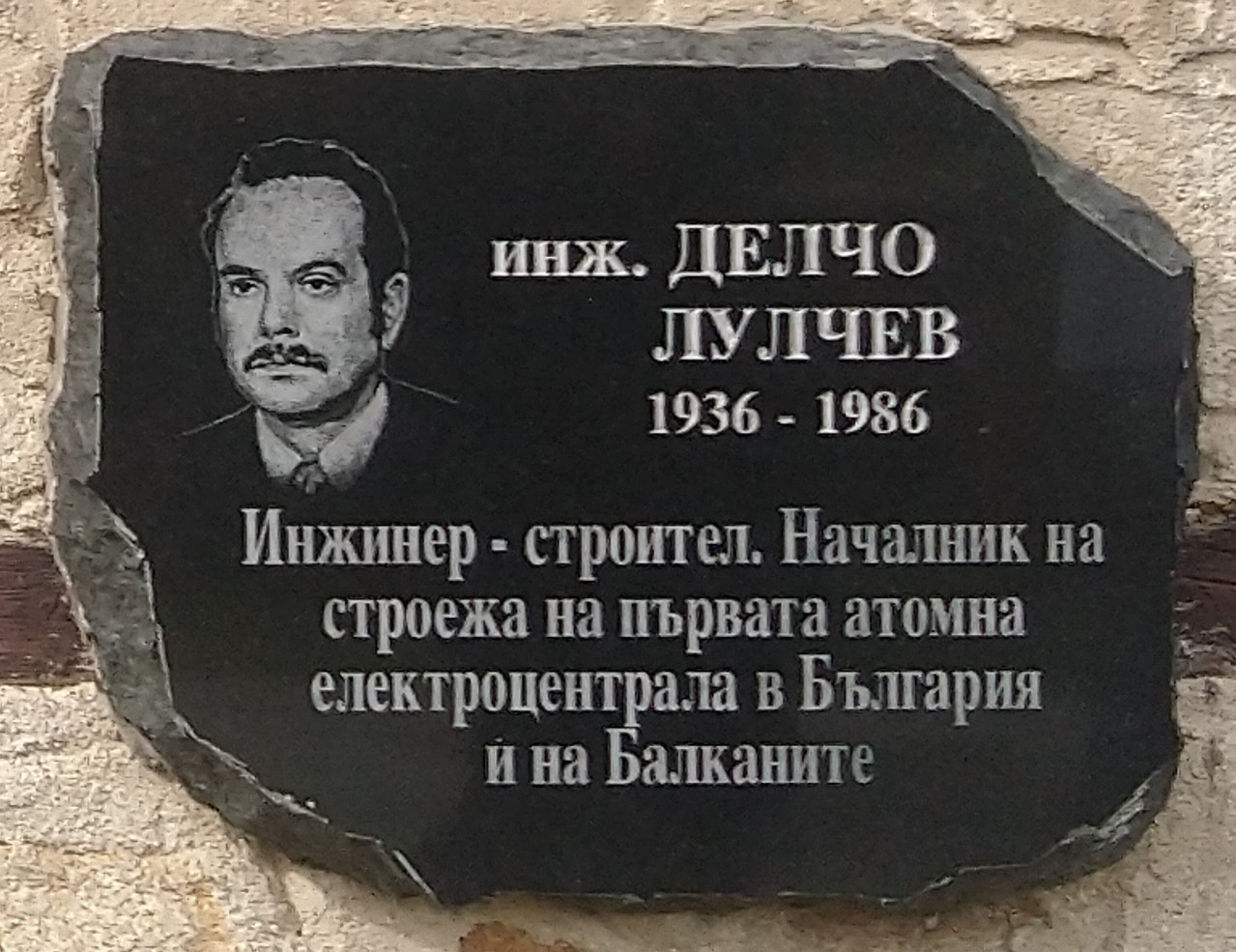 Черна паметна плоча с гравиран портрет на мъж с мустаци и надпис „инж. Делчо Лулчев 1936–1986, инженер-строител“.